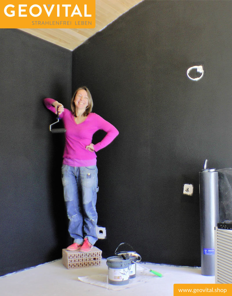 Frau steht vor schwarz gestrichener Wand mit T98 Abschirmfarbe
